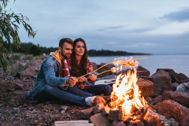 happy couple roasting marshmallows on sticks near bonfire  clipart