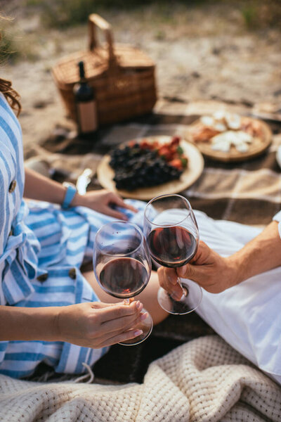cropped view of couple clinking glasses with red wine 