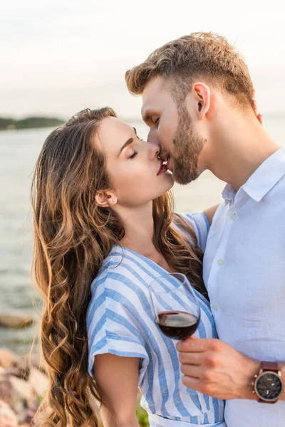 髭を生やした男が彼女にキスして湖の近くで赤ワインでグラスを持ち — ストック写真