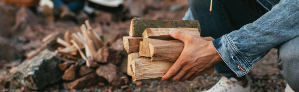 panoramic shot of man in denim jacket holding firewood in hands