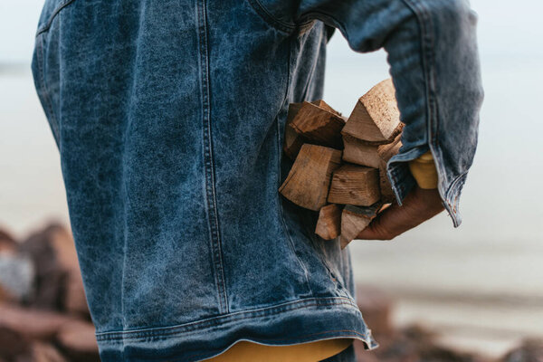 cropped view of man in denim jacket holding firewood 