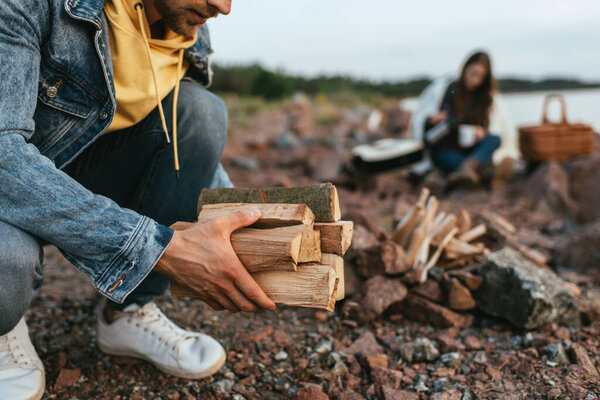 cropped view of man in denim jacket holding firewood near girl 