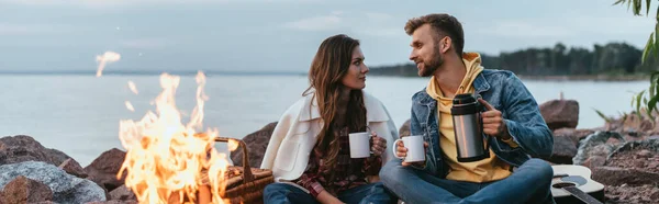 Panoramic Shot Couple Holding Cups Sitting Bonfire Lake — Stock Photo, Image