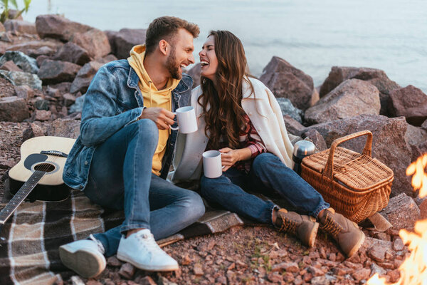 selective focus of happy woman laughing near boyfriend with cup of tea