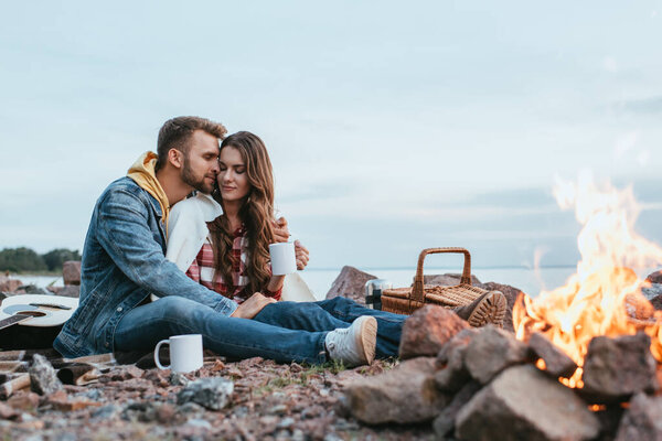 selective focus of happy man hugging attractive girl with cup near bonfire