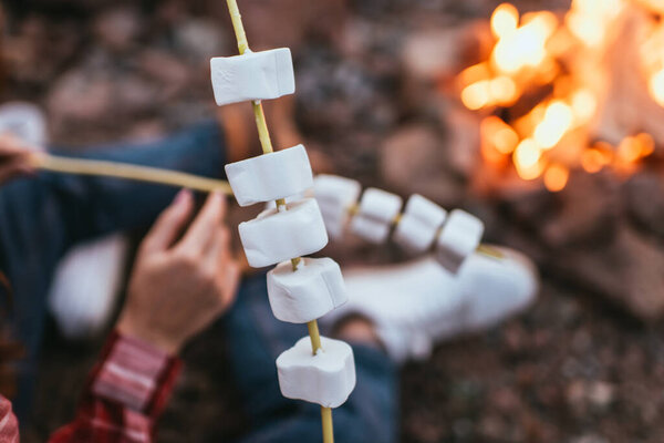 selective focus of puffy marshmallows on sticks near couple and bonfire