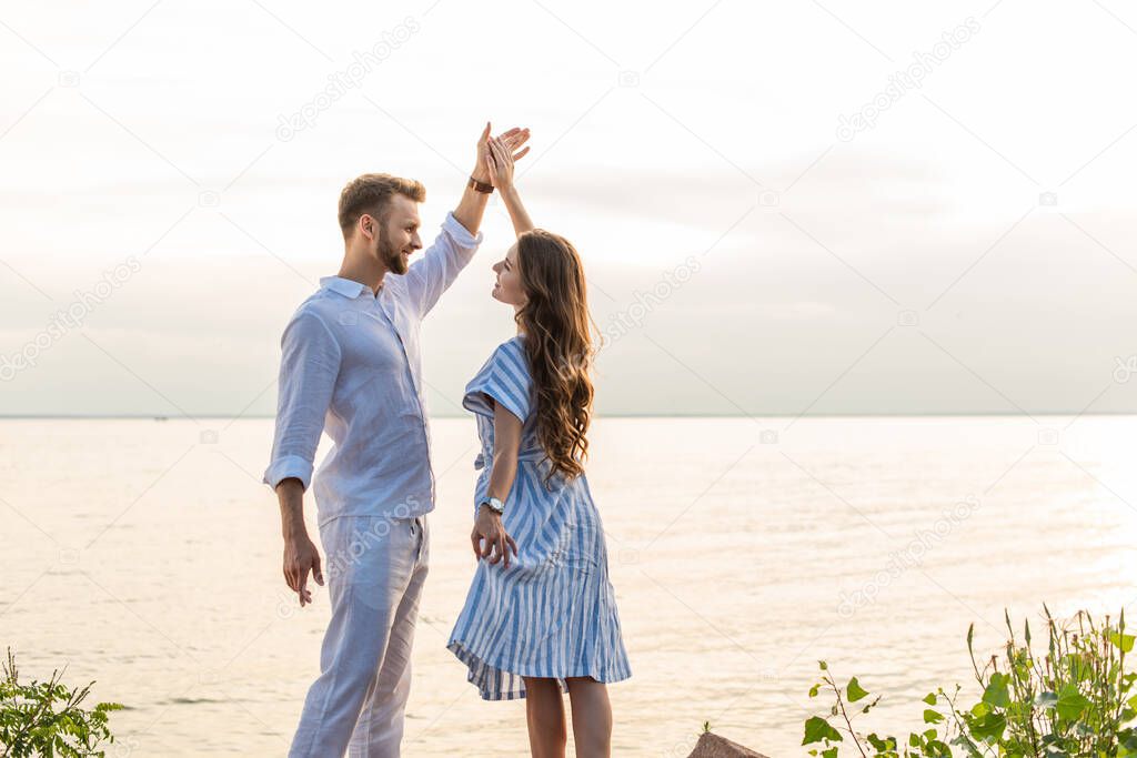 cheerful couple holding hands and dancing near lake 