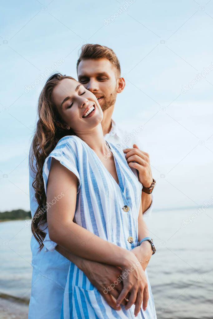 bearded man smiling and hugging cheerful girl near lake