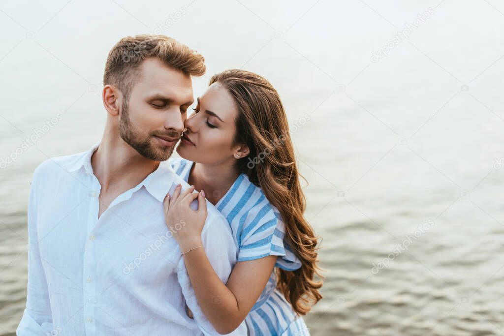 attractive woman hugging handsome man with closed eyes near river 