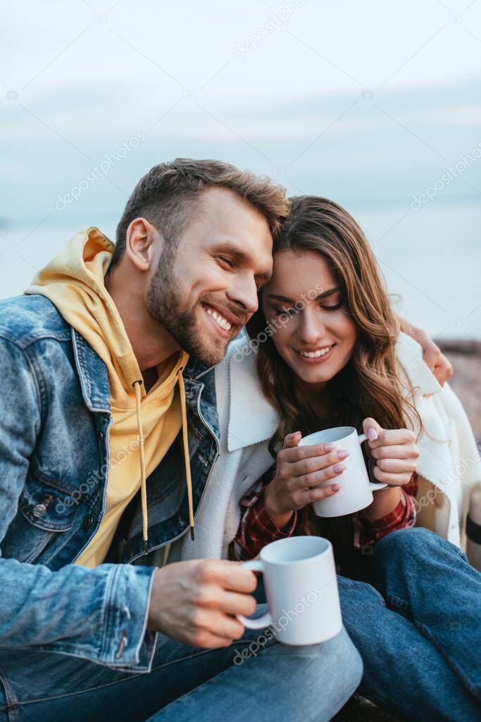 happy man hugging cheerful young woman and holding cup of tea