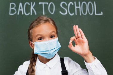 Tıbbi maskeli kız öğrencilerin seçici odak noktası okula geri döndüğümüzde karatahtaya yazılmış iyi bir jest olduğunu gösteriyor.