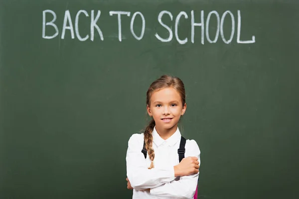Smiling Schoolgirl Standing Crossed Arms Chalkboard Back School Inscription — Stock Photo, Image