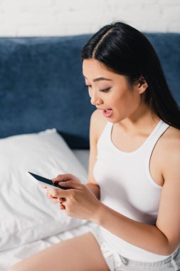 Şok olmuş Asyalı kadın elinde boş ekranla akıllı telefon tutuyor. 