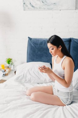 Evde yatakta otururken akıllı telefon kullanan Asyalı kız şaşırdı. 