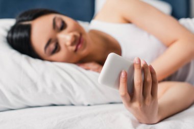 Asyalı kadının yatakta akıllı telefon kullandığı seçici odak noktası 