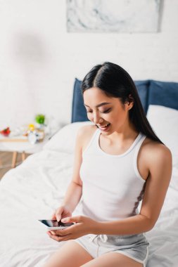 Güzel Asyalı kız evde yatarken akıllı telefon kullanıyor. 