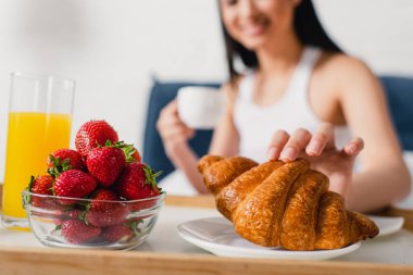 Çileklerin yanında kruvasan ve kahvaltı tepsisinde bir bardak portakal suyu içen seçici bir kadın. 