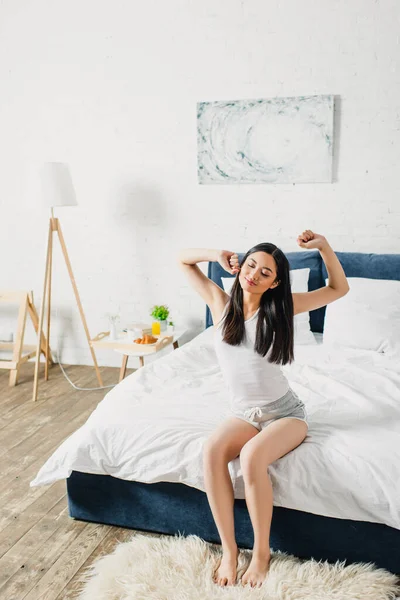 Glimlachende Aziatische Vrouw Stretching Terwijl Zitten Bed Ochtend — Stockfoto
