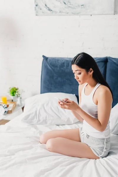 Sorprendido Asiático Chica Usando Smartphone Mientras Sentado Cama Casa — Foto de Stock