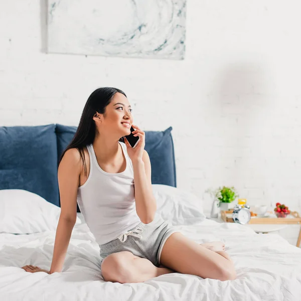 아름다운 소녀가 아침에 침대에서 스마트폰으로 이야기하는 — 스톡 사진