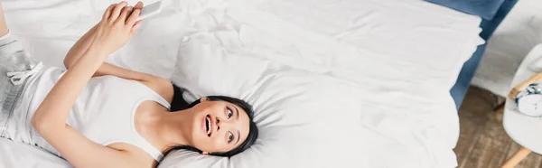 Panoramic Shot Positive Asian Girl Holding Smartphone Looking Away Bed — Stock Photo, Image