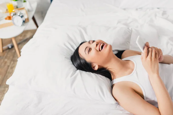 Vysoký Úhel Pohledu Smějící Asijské Žena Drží Smartphone Při Ležení — Stock fotografie