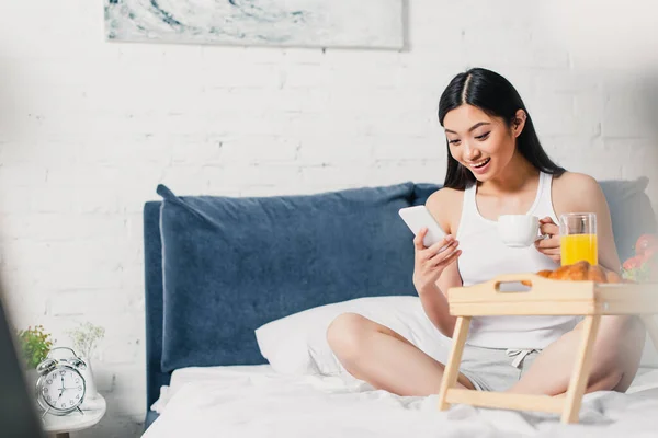 Selective Focus Smiling Asian Girl Using Smartphone Holding Coffee Cup — Stock Photo, Image