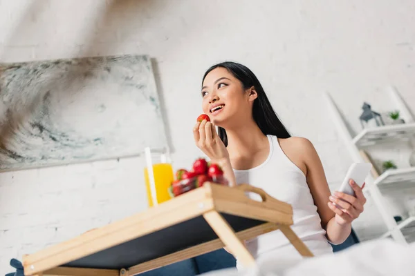 Selective Focus Smiling Asian Girl Holding Strawberry Smartphone Breakfast Bed — Stock Photo, Image