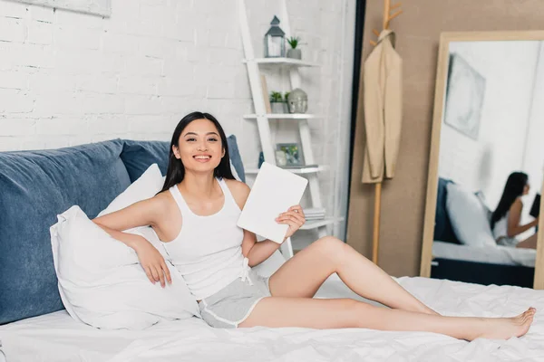 Красива Азіатська Жінка Тримає Цифровий Планшет Посміхається Камеру Ліжку Вдома — стокове фото