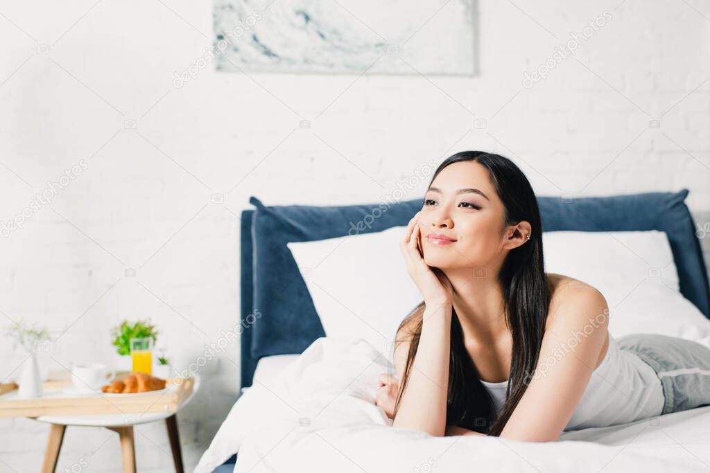 Beautiful asian woman looking away while lying on bed at morning 