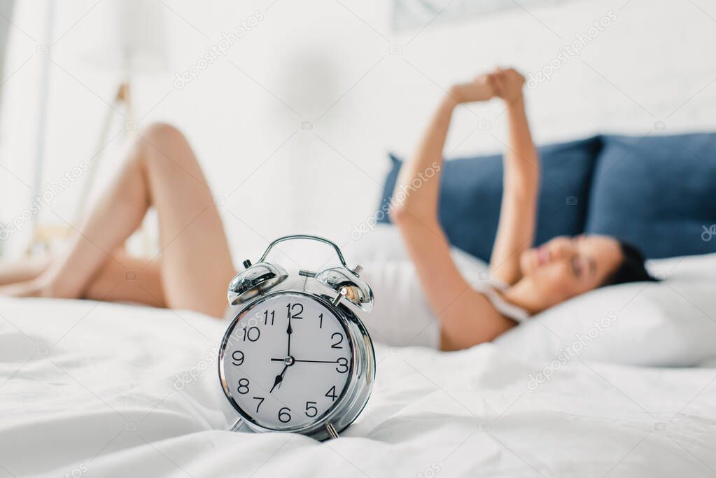 Selective focus of alarm clock and young woman lying on bed at morning 