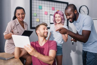 Selective focus of african american businessman pointing with finger at digital tablet near colleagues in office  clipart