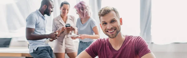 Foto Panorâmica Empresário Olhando Para Câmera Enquanto Colegas Multiétnicos Conversando — Fotografia de Stock