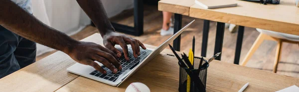 事務所の文房具や野球ボールの近くのラップトップを使用してアフリカ系アメリカ人ビジネスマンのパノラマの向き — ストック写真