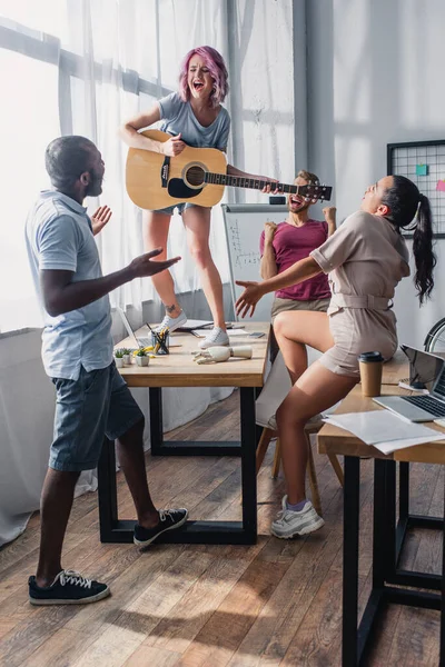 オフィスでアフリカ系アメリカ人の同僚を見て音響ギターを持つビジネス女性の選択的な焦点 — ストック写真