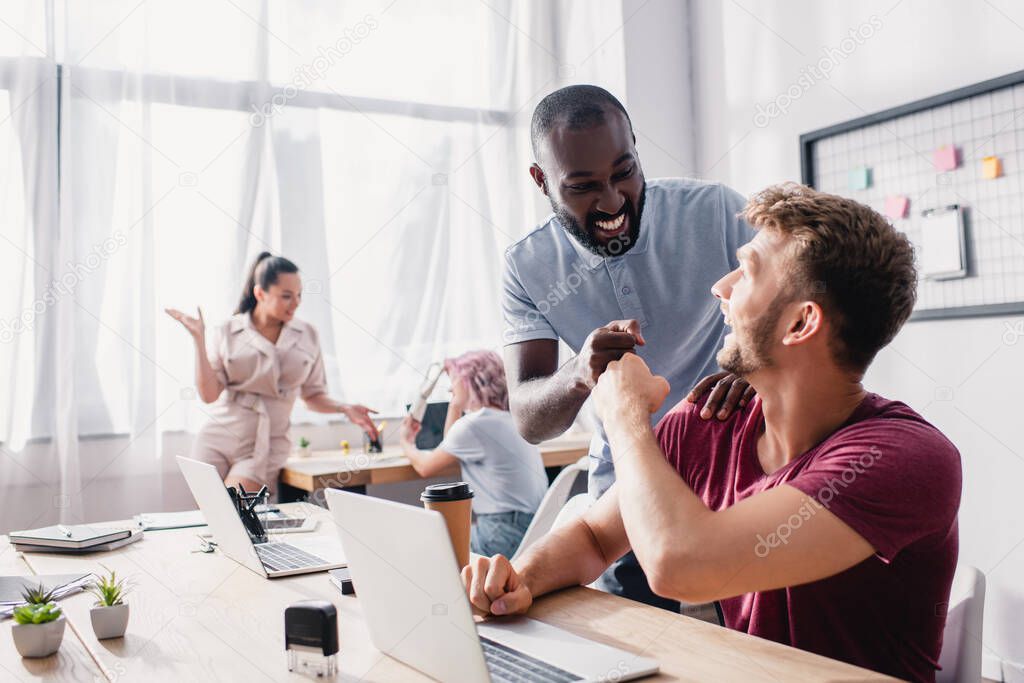 Selective focus of multicultural businessmen doing fist bump while working in office 