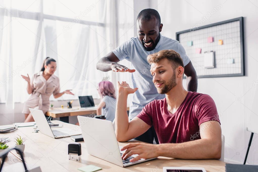 Selective focus of businessman giving high five to african american colleague in office 