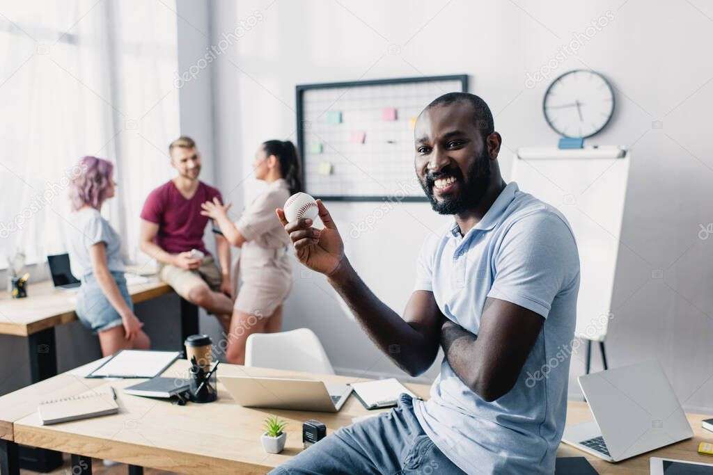 Selective focus of african american businessman holding baseball ball in office 