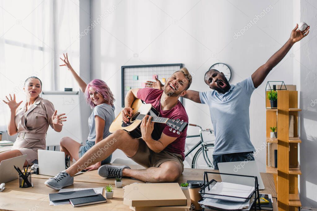 Young multiethnic business people singing and playing acoustic guitar in office 