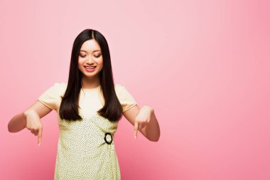 Neşeli Asyalı kız parmaklarıyla işaret ediyor ve pembe üzerine izole bir şekilde bakıyor. 