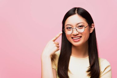 happy asian girl pointing with finger at glasses isolated on pink  clipart