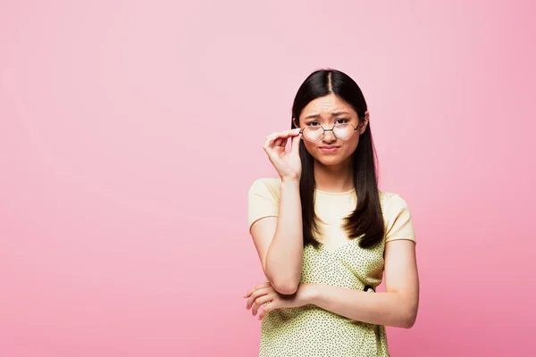 不满意的亚洲女孩看着相机和用粉色隔离的触摸眼镜 — 图库照片