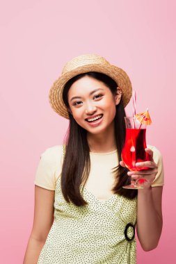 Hasır şapkalı gülümseyen Asyalı kadın pembe bardakta kokteyl tutuyor.