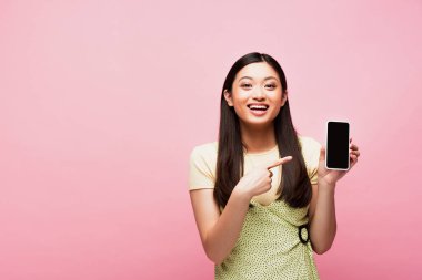 Pozitif Asyalı kadın pembe ekranda boş ekranlı akıllı telefonu işaret ediyor. 