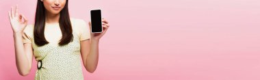 Pembe ekranda boş ekranlı akıllı telefonu tutarken ok işareti gösteren panoramik bir kadın mahsulü. 