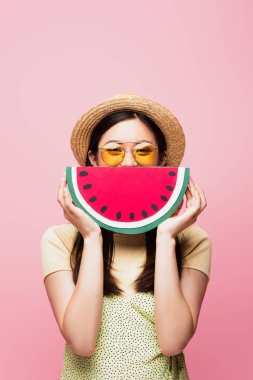 Güneş gözlüklü Asyalı kadın ve hasır şapkalı yüzü pembe karpuzla kaplı. 