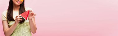 Pembe üzerine izole edilmiş dilimlenmiş kağıt karpuz tutan pozitif kızın panoramik mahsulü 