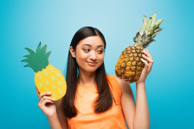 Mutlu Asyalı kız olgun ve mavi üzerine karton ananas tutuyor. 