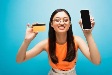 Mutlu Asyalı kız elinde akıllı telefon, elinde boş ekran ve mavi kart var. 