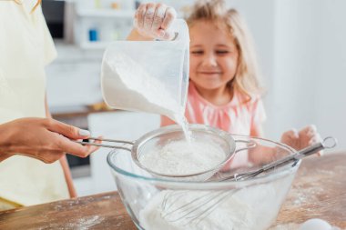 Kızı cam kaseye çiçek koyarken elek tutan kadının kısmi görüntüsü, seçici odaklanma  